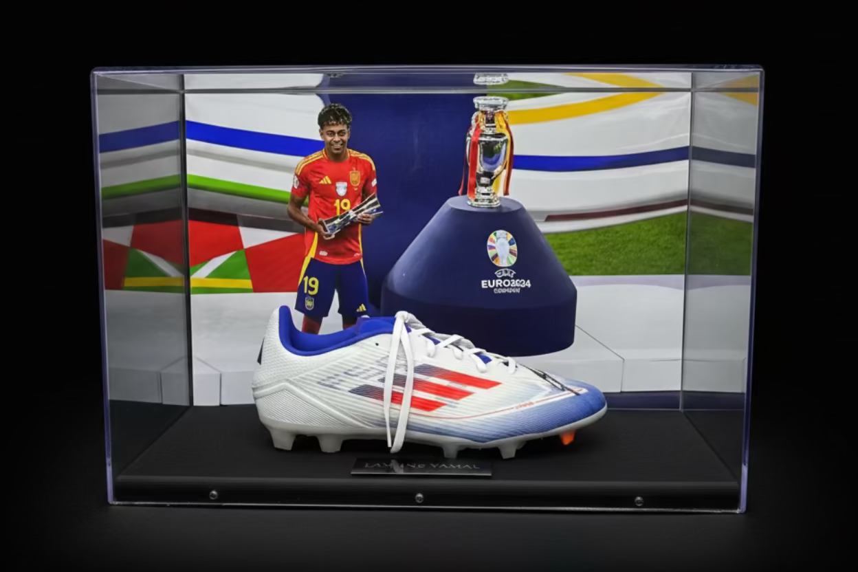 Display case with soccer boot and trophy on a sports field background